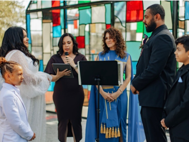 A wedding blessing before a stained-glass wall